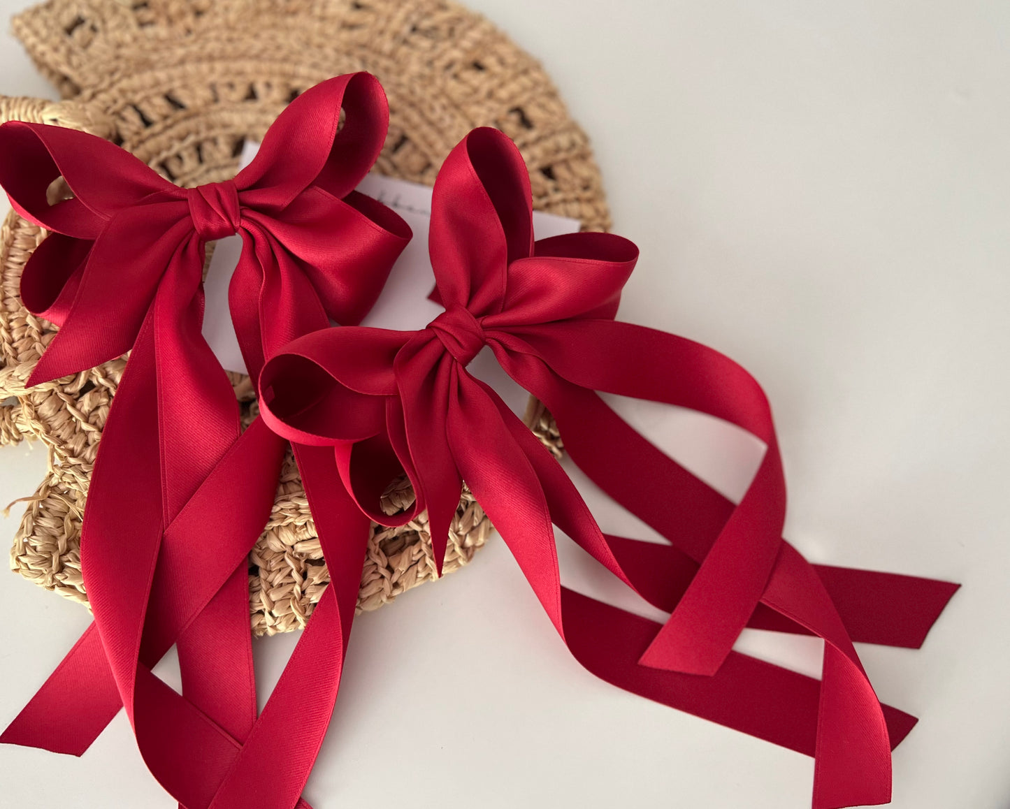 A red satin hair bow with a twist design, displayed on a woven hat.